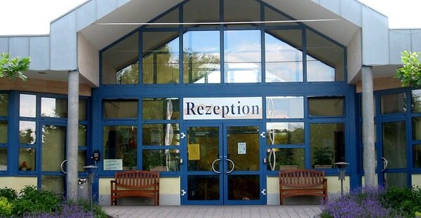 Eingangsbereich eines Hotels mit großer Glasfront und dem Schild „Rezeption“ über der Tür.