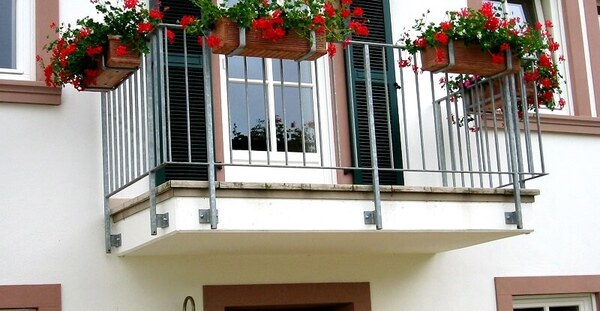 Kleiner Balkon mit Metallgeländer und Blumenkästen mit roten Geranien am Haus.