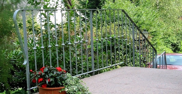 Metallgeländer an einer Außentreppe mit Blumen und grüner Gartenbepflanzung im Hintergrund.
