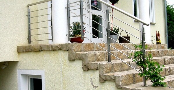 Eingangsbereich mit Steintreppe und modernem Edelstahlgeländer vor einem Haus.