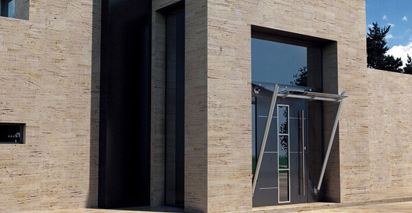 Moderne Eingangstür mit Glasvordach an einer Fassade aus Naturstein in zeitgemäßem Design.